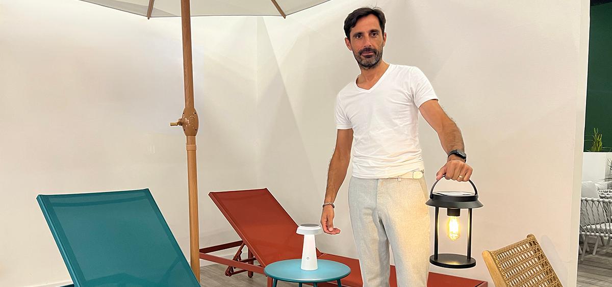 Modern outdoor lighting designed by NBHanyuan Lighting features a man standing next to outdoor furniture displaying a black portable lamp. The scene includes lounge chairs, side tables and umbrellas, creating a modern and minimalist outdoor lounge atmosphere.