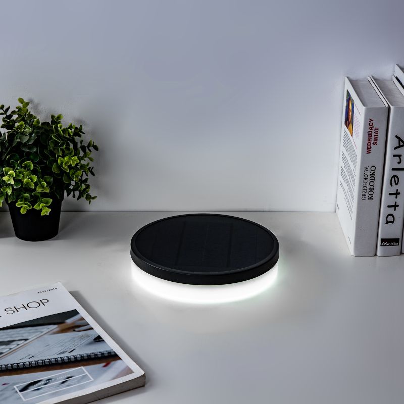 NB Hanyuan solar-powered Lumibox round lamp placed on a concrete surface near a swimming pool, with visible solar panel and attached wire, surrounded by green grass.