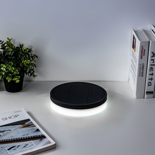 NB Hanyuan solar-powered Lumibox round lamp placed on a concrete surface near a swimming pool, with visible solar panel and attached wire, surrounded by green grass.