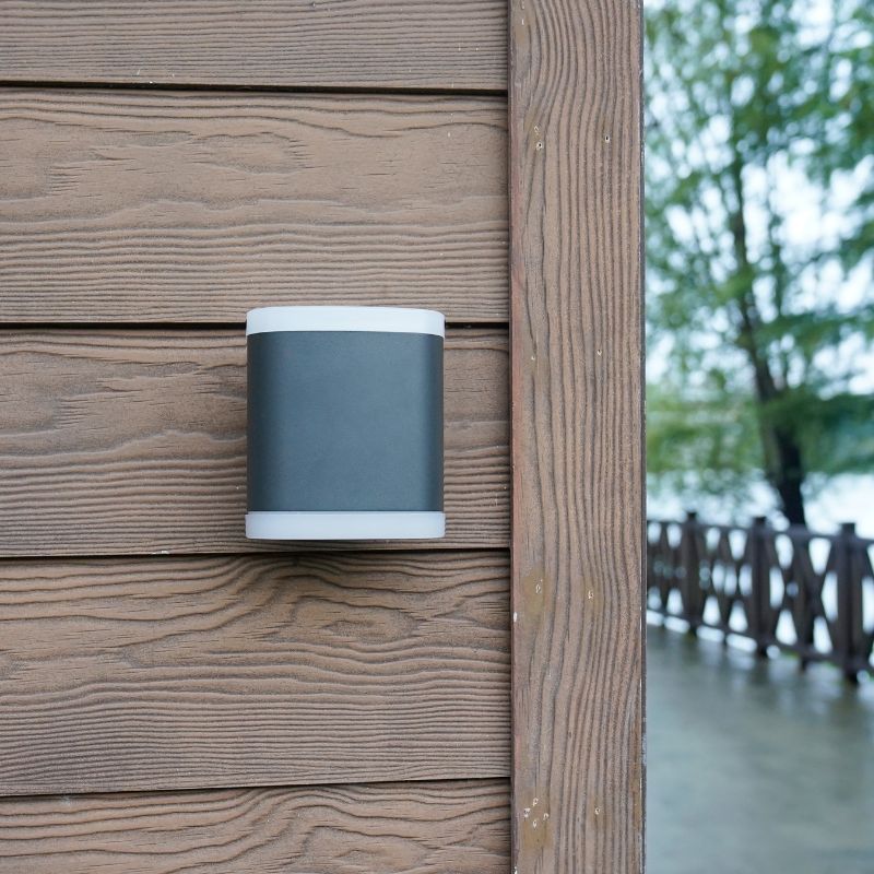 A modern black and white outdoor wall lamp with a cylindrical design, mounted on a wooden wall, perfect for enhancing exterior lighting with a sleek, contemporary look.